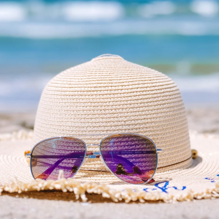 Sunglasses next to a hat on a beach background